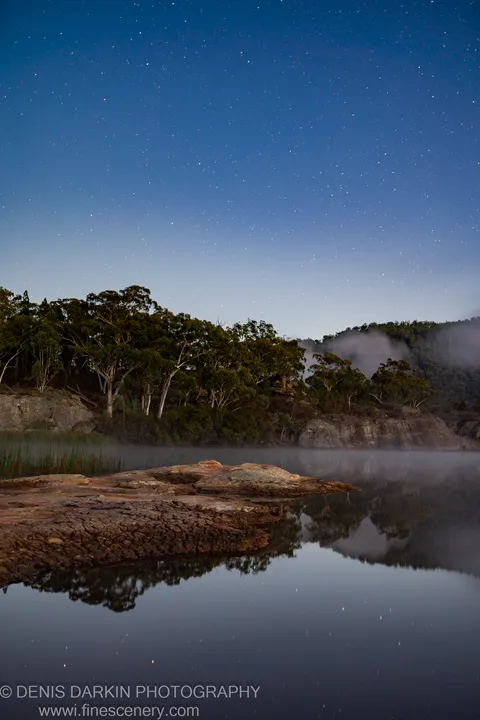 A star-flecked sky arches over Dunns Swamp at dawn, mist drifting along the banks past lichen-covered sandstone outcroppings.
