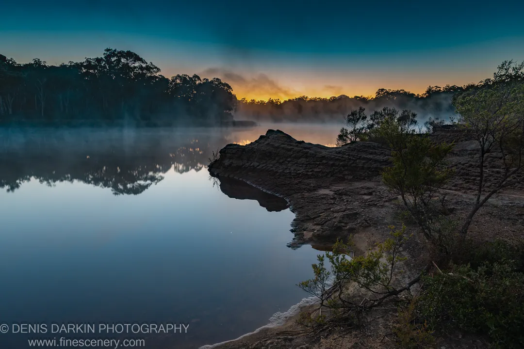 A stratified sandstone formation on the right bank catches the early dawn colour above the mist-covered water at Dunns Swamp.