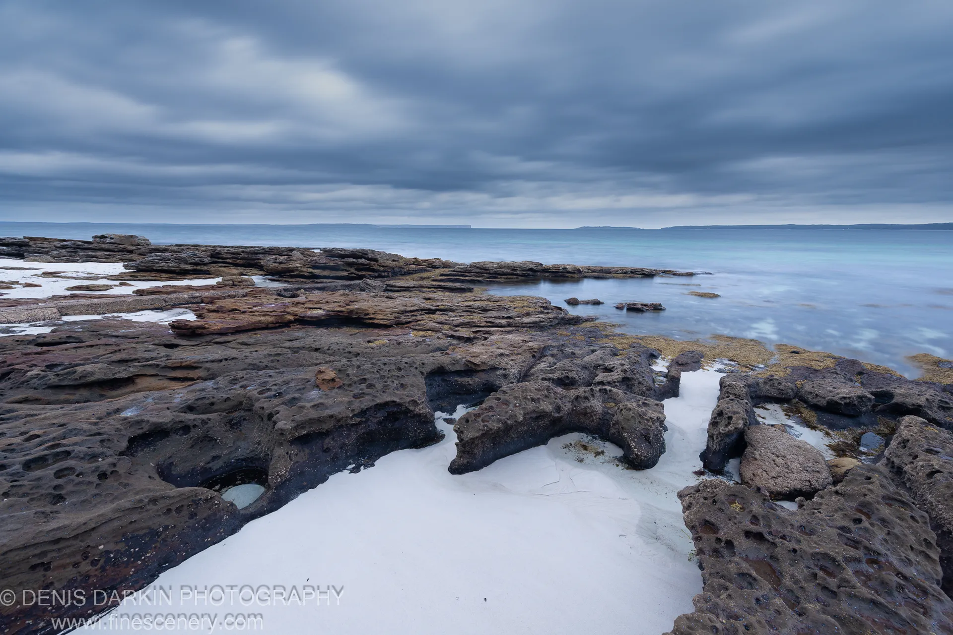 Pockmarked sandstone rock shelf with foam-filled pools at Huskisson, New South Wales, under an overcast predawn sky in December 2019.