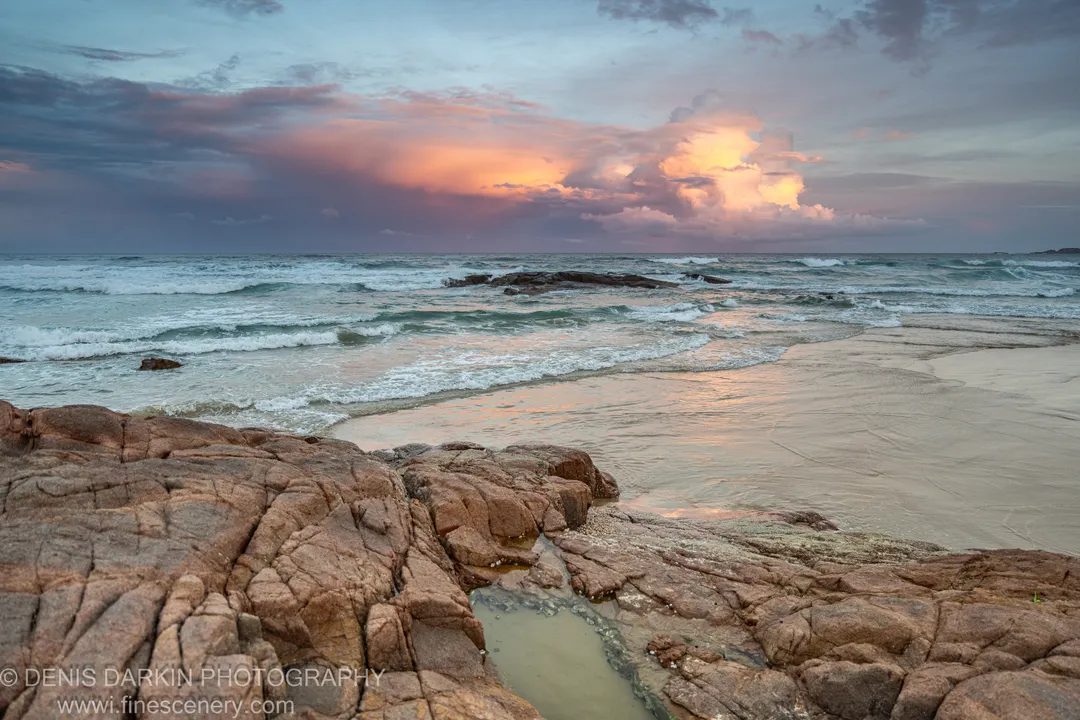 Fissured rock formations in the foreground lead toward a cloud-lit horizon over the rocky shoreline at One Mile Beach, Port Stephens.