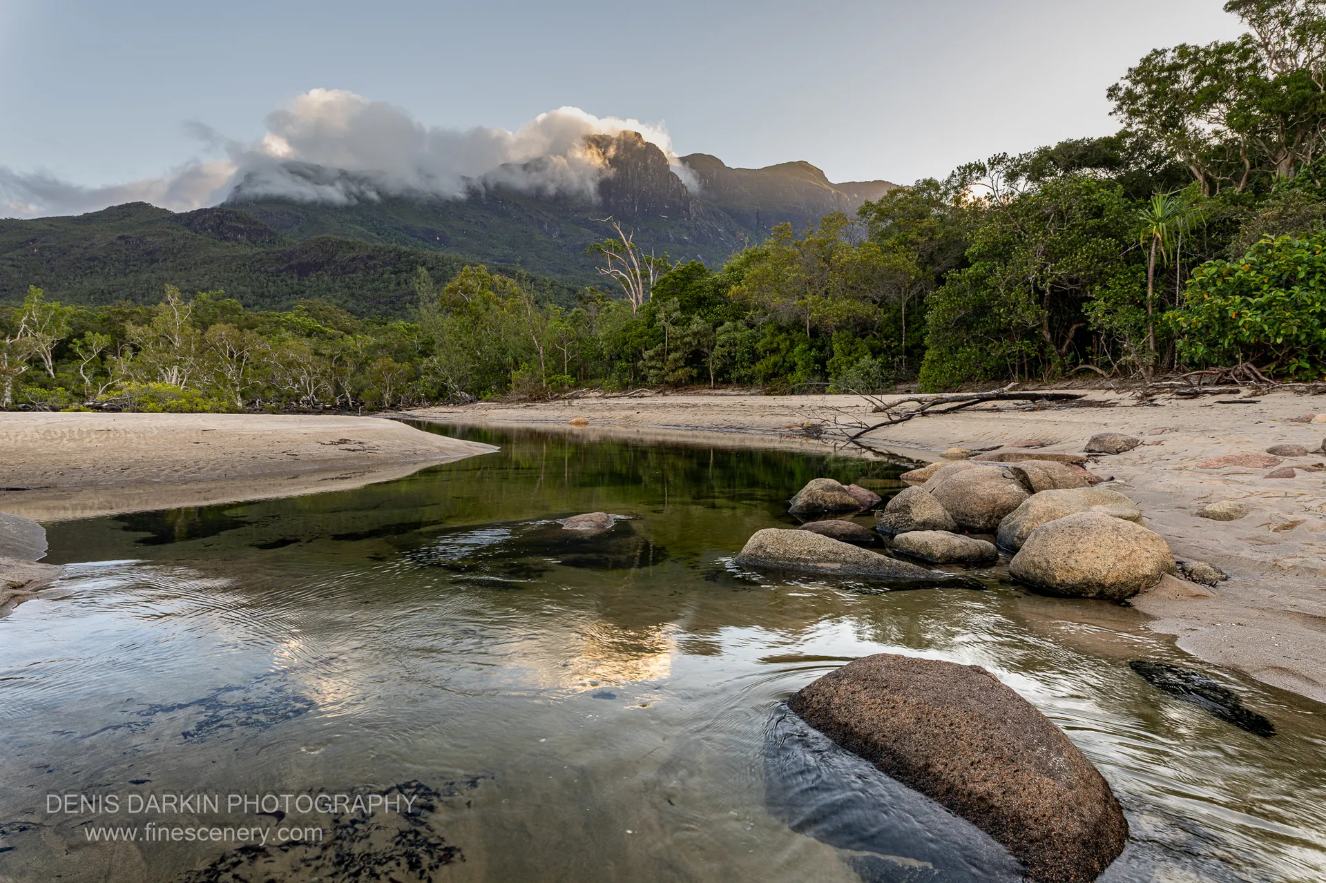 Shallow tidal creek at Little Ramsey Bay reflecting a cloud-wrapped granite ridge, with rounded granite boulders along the sandbar in low sun.