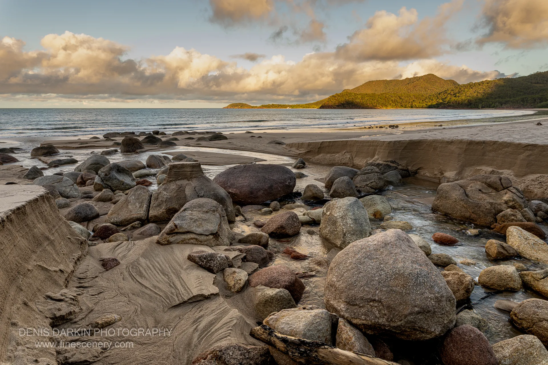 Granite boulders and a shallow tidal creek at Little Ramsey Bay lead toward a forested headland lit by low evening sun.
