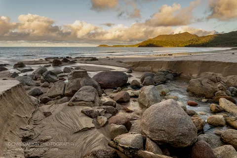 Granite boulders and a shallow tidal creek at Little Ramsey Bay lead toward a forested headland lit by low evening sun.