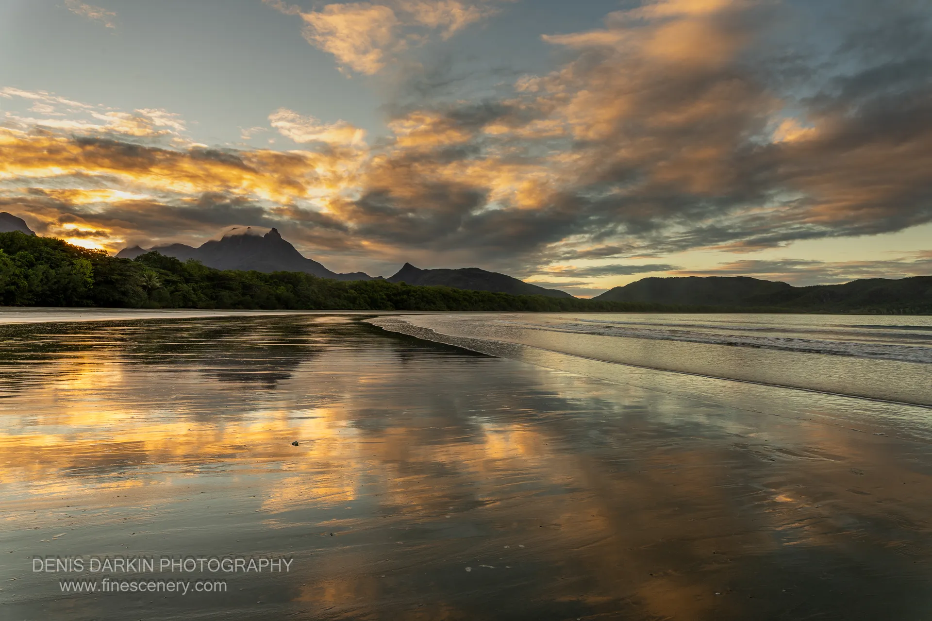 Receding water on the wide tidal flat of Zoe Bay mirrors orange-lit cloud at sunset, with a cloud-shrouded peak beyond.