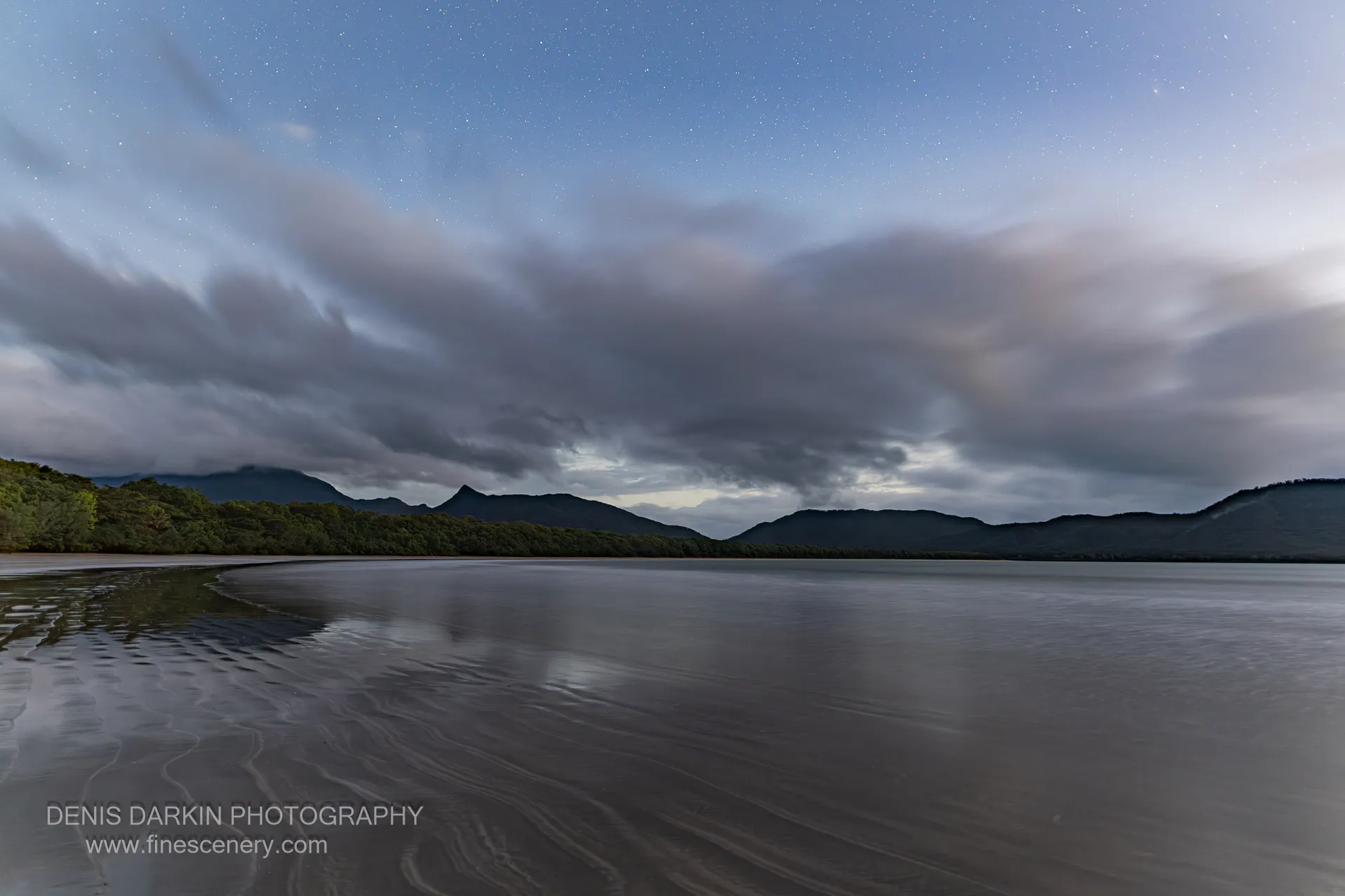 Before dawn at Zoe Bay, a long exposure smooths the tidal flat and bay beneath a heavy cloud bank drifting over low ranges.