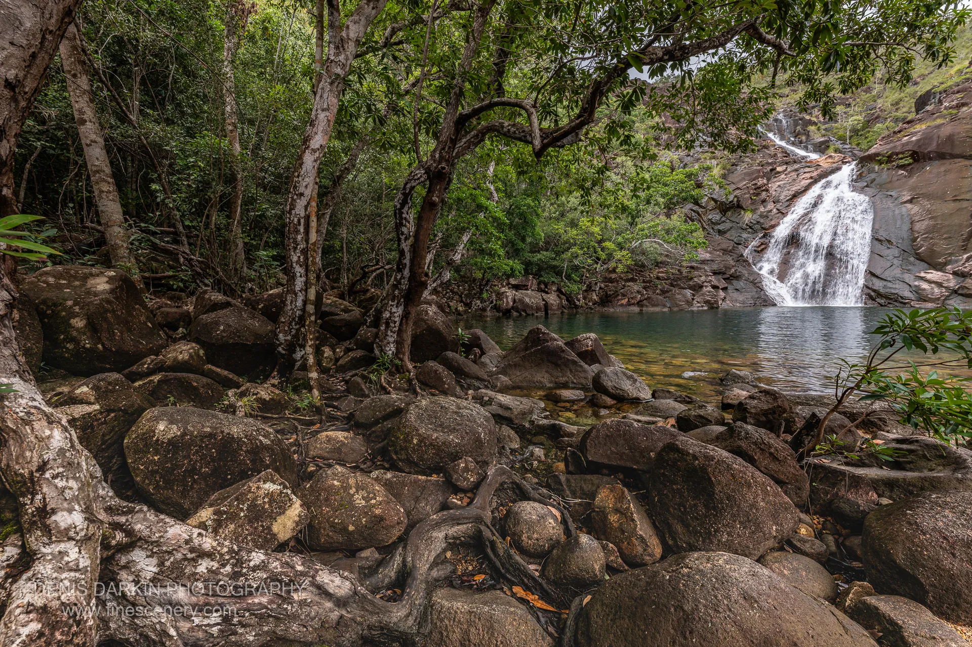 Zoe Falls slides down a broad granite face into a clear green plunge pool ringed by boulders and rainforest on Hinchinbrook Island.