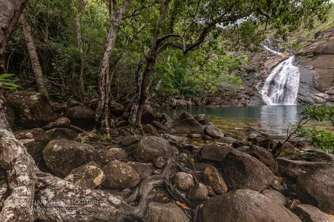 Zoe Falls slides down a broad granite face into a clear green plunge pool ringed by boulders and rainforest on Hinchinbrook Island.