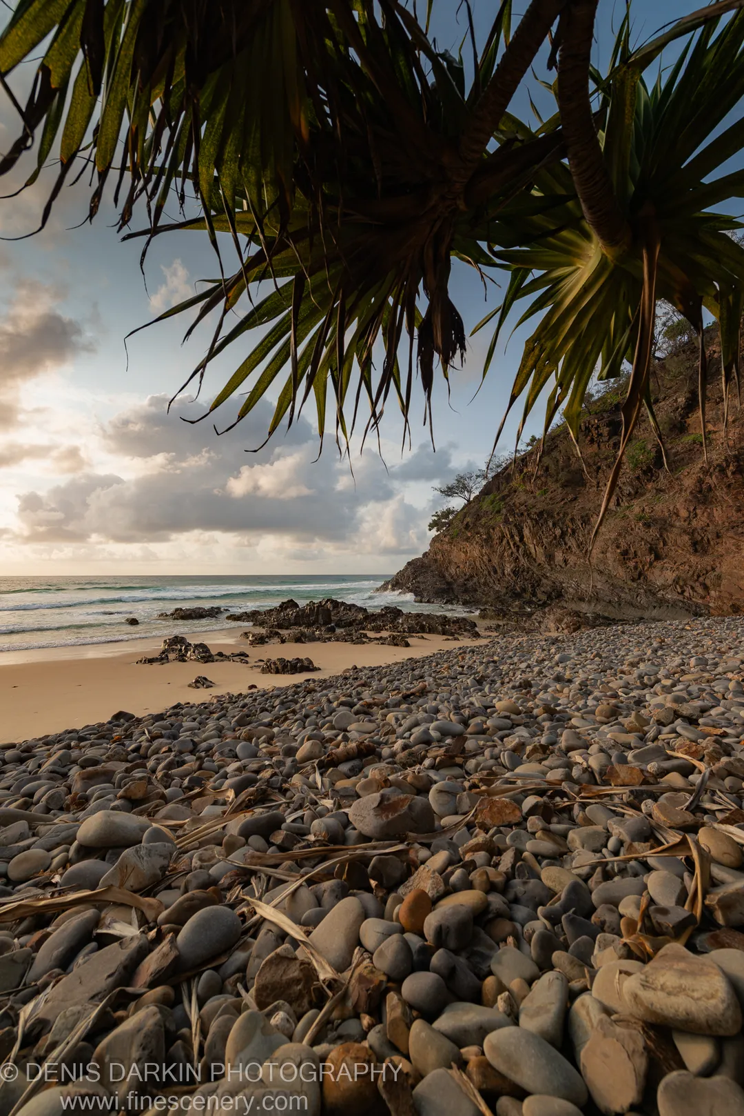 Soft dawn light over a calm ocean cove with pebble beach and rocky headland on the Queensland coast, January 2020.