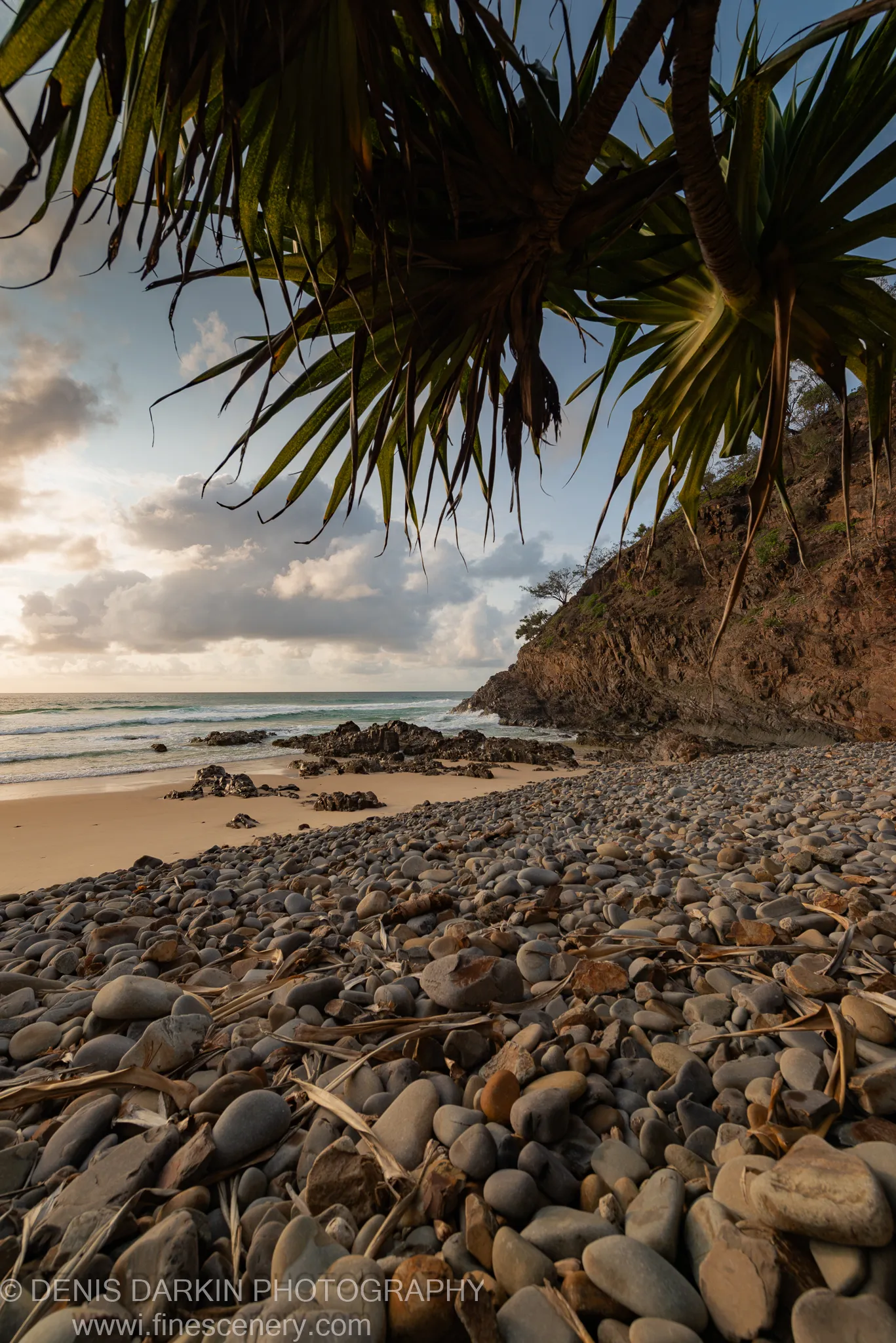 Soft dawn light over a calm ocean cove with pebble beach and rocky headland on the Queensland coast, January 2020.