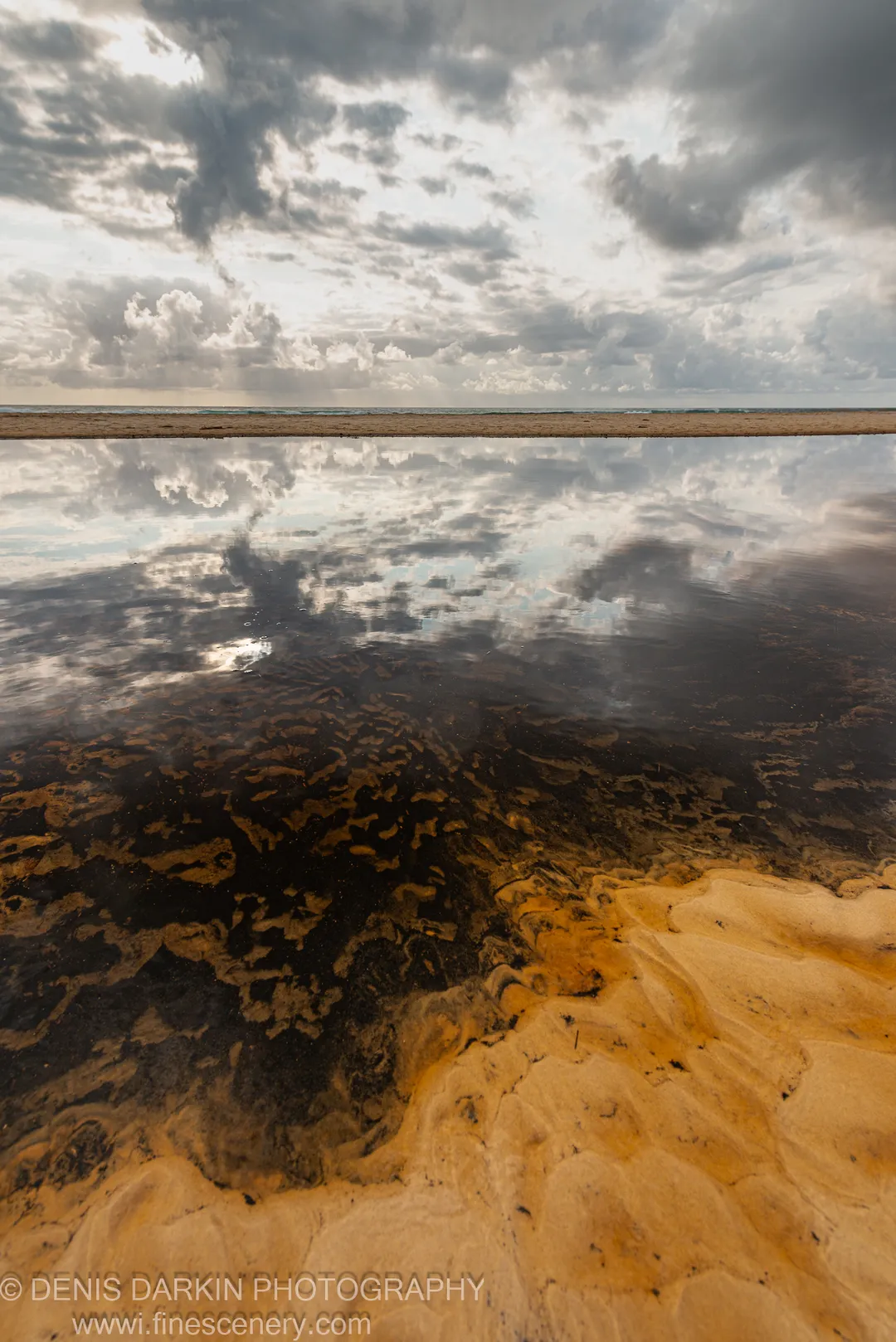 A tidal flat on the Queensland coast at dawn, with storm clouds and their near-perfect reflection in the still, shallow water below.
