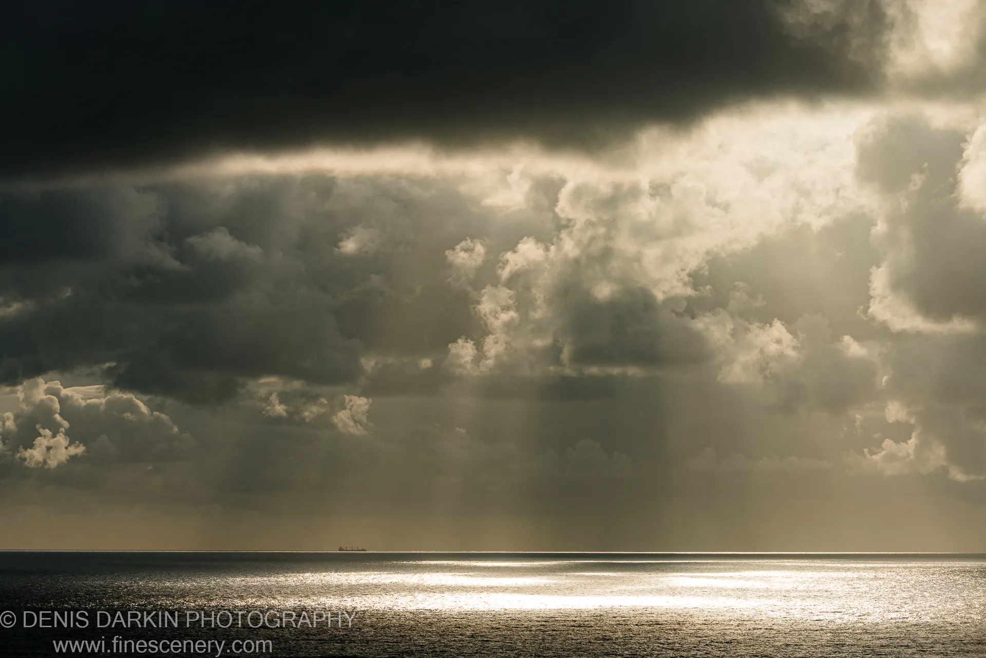 Heavy cumulus clouds at dawn over the Queensland coast, with crepuscular rays reflecting on the water and a distant ship on the horizon.