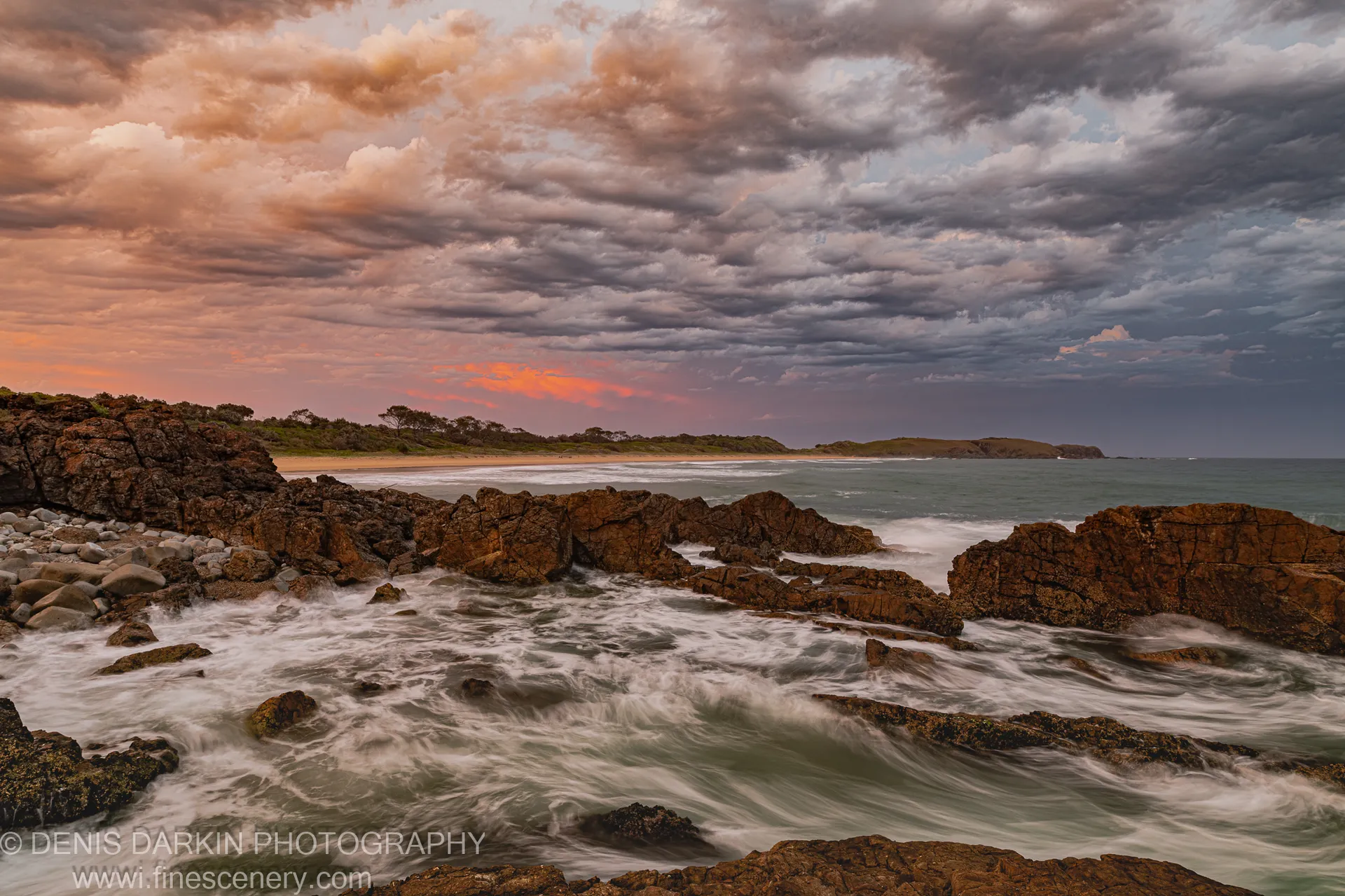 Rocky outcrops and long-exposure water at predawn near Coffs Harbor, with wet sand reflections and islands silhouetted against the brightening horizon.