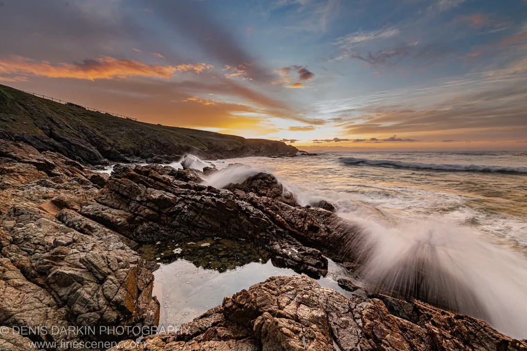 Layered sandstone cliffs and a coastal rock pool before sunrise on the New South Wales coast, smooth long-exposure surf below.