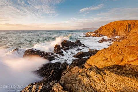 Layered sandstone cliff face in morning light above long-exposure surf and dark rocks at the Coffs Harbor coast, October 2020.