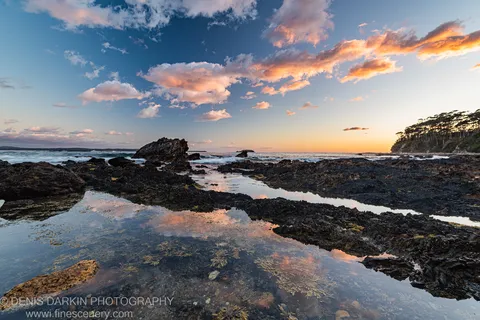 Shallow tidal pools on a basalt rock platform reflect a pink and azure dawn sky on the South Coast of New South Wales.
