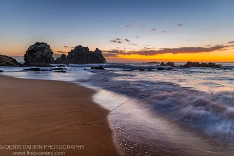 Sea stacks silhouetted against a predawn horizon on the South Coast, with blurred wave motion on wet sand.