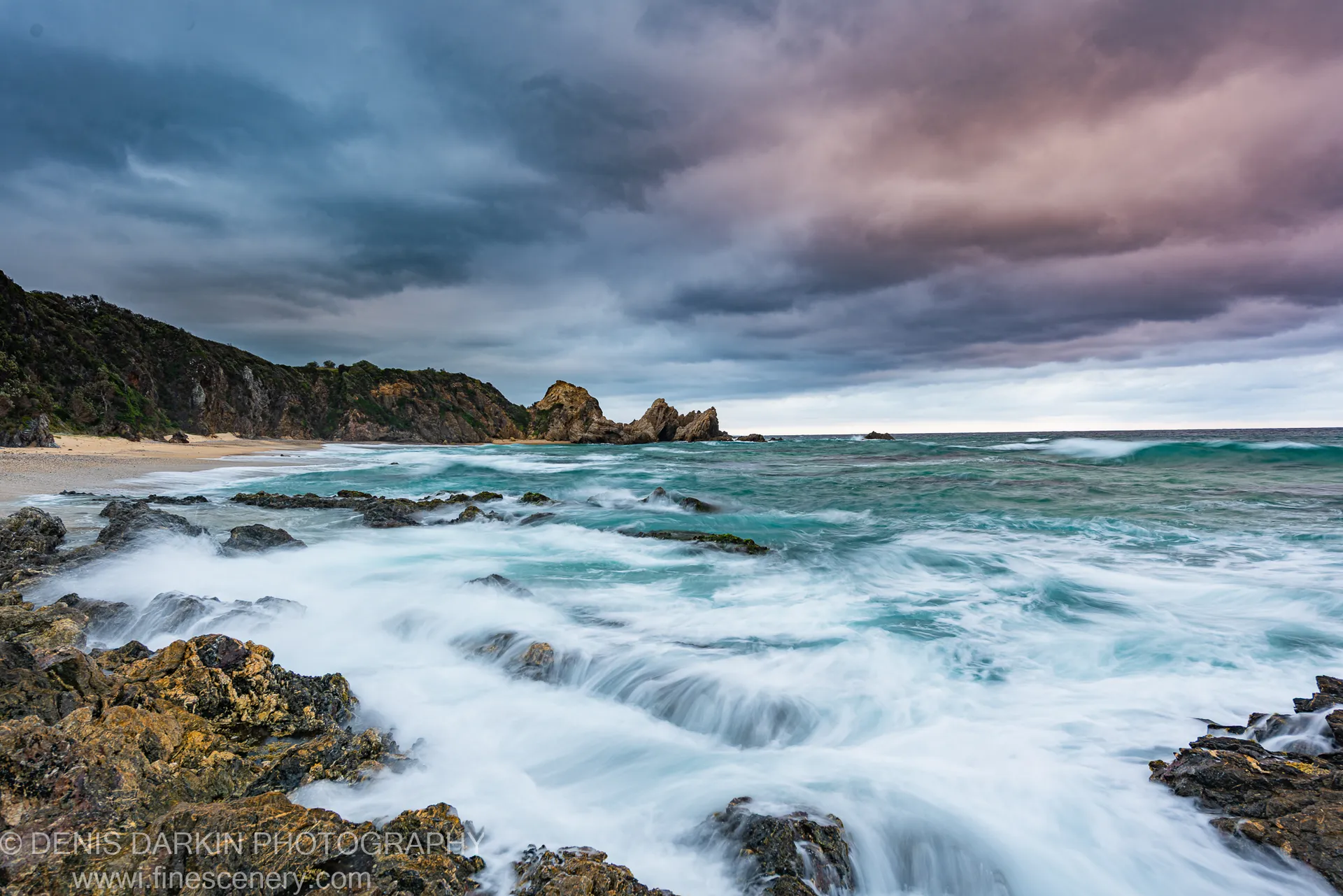 Long-exposure waves break against sea-stacks in a storm-lit cove on the New South Wales South Coast at dawn.