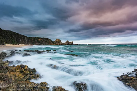 Long-exposure waves break against sea-stacks in a storm-lit cove on the New South Wales South Coast at dawn.