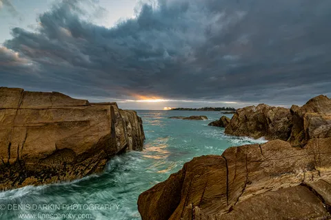 Layered sandstone formations border a coastal channel of turquoise water on the NSW South Coast, with sunrise light on the horizon.