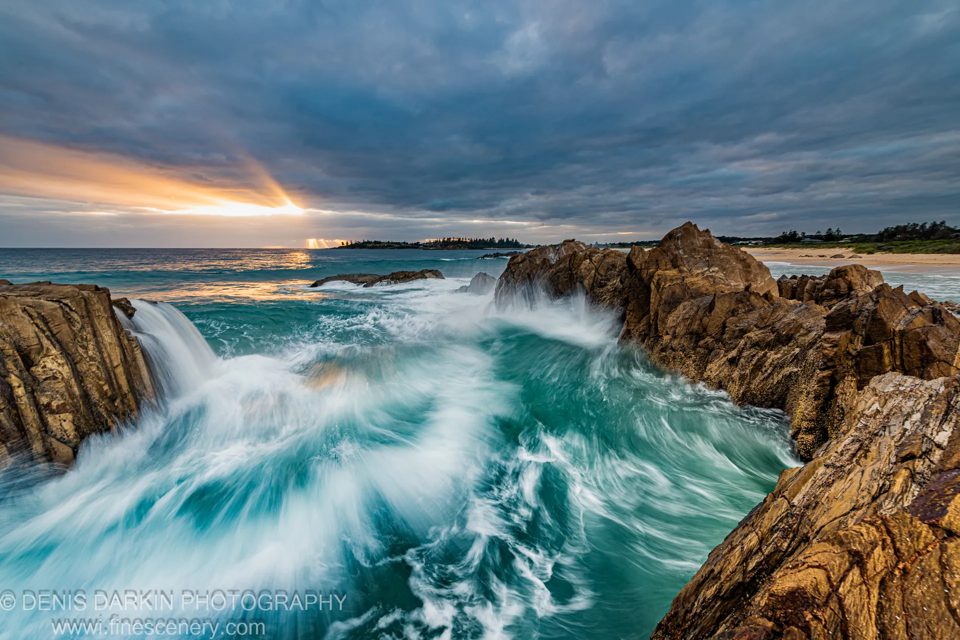 A bright sunburst breaks through heavy storm clouds over the South Coast of NSW, casting warm light across the ocean below at dawn.