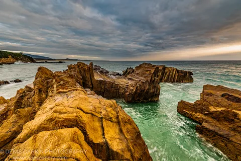 Rock ledges with warm tonal highlights border a surge channel through which turquoise water swirls at dawn, New South Wales South Coast, December 2020.