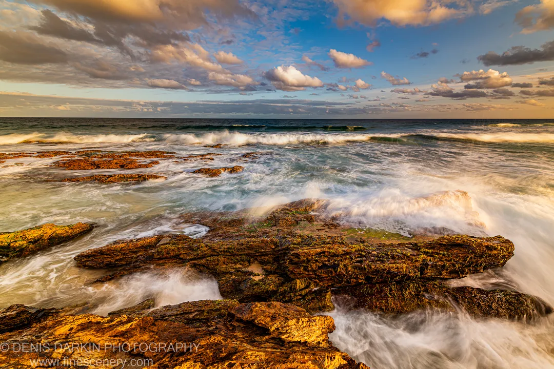 Algae-covered reef on the New South Wales South Coast, long-exposure waves reduced to white streaks around dark formations at dusk.