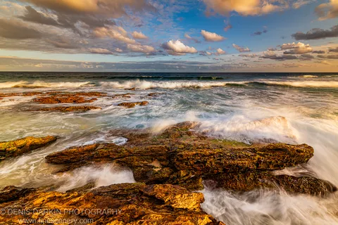 Algae-covered reef on the New South Wales South Coast, long-exposure waves reduced to white streaks around dark formations at dusk.