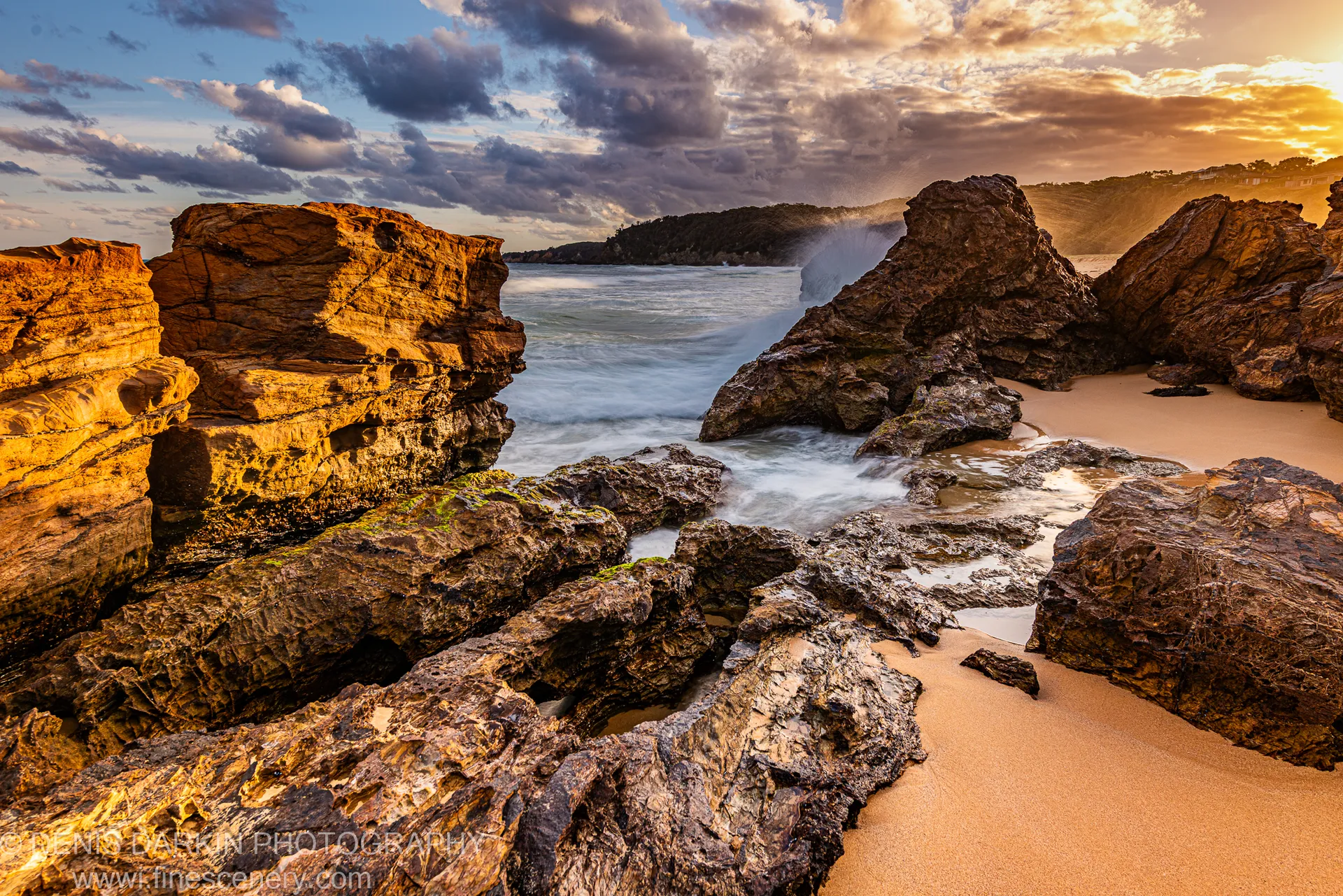 Sandstone rock formations opening to a sheltered pocket beach with misty, slow-shutter surf on the New South Wales South Coast at dusk.
