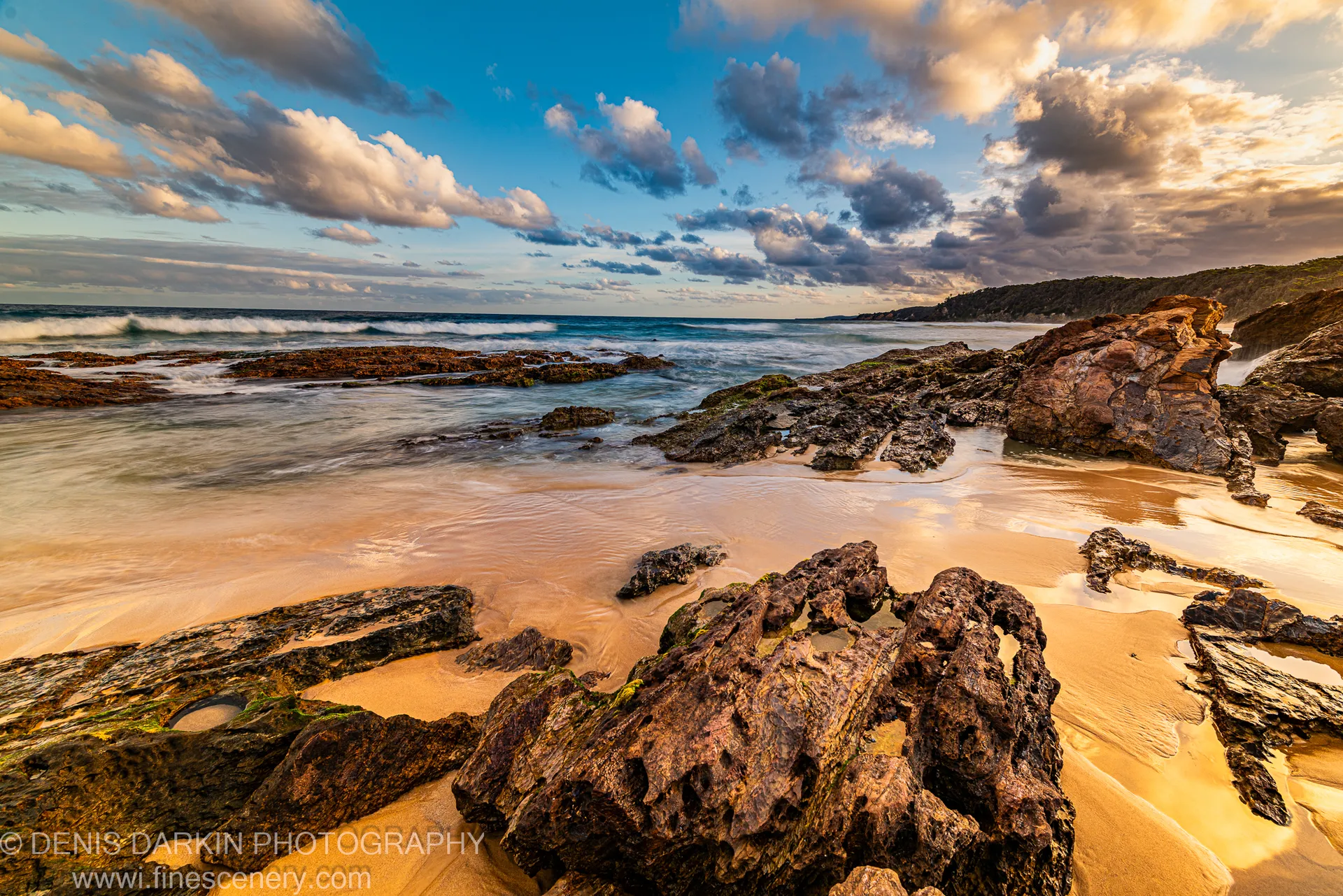 Warm dusk light on a rocky beach and tidal channel on the New South Wales South Coast, long-exposure mist around pitted volcanic rock.