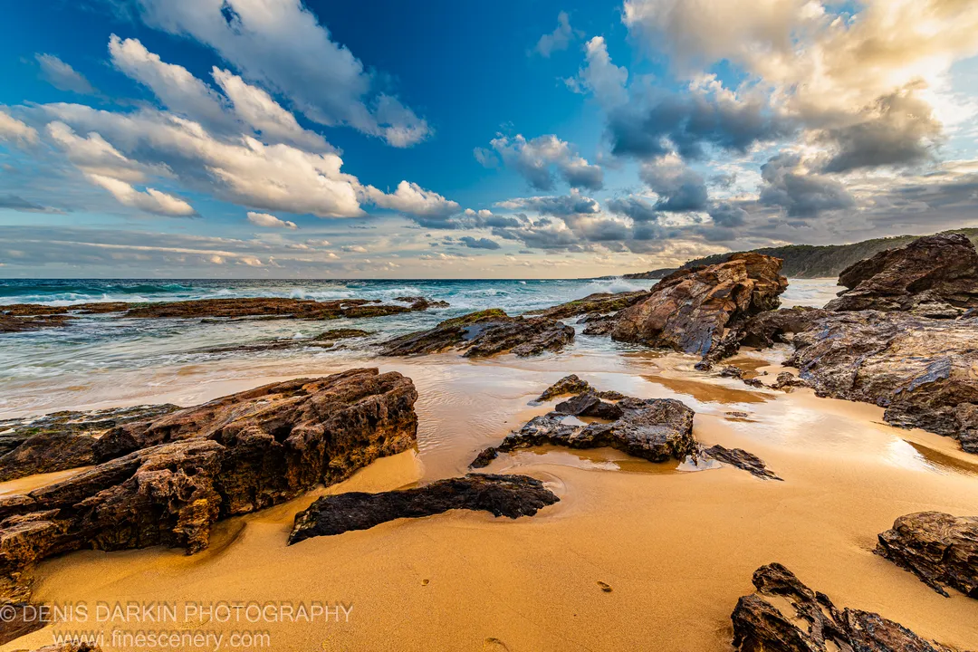 Deep blue sky with cumulus clouds above turquoise waves breaking on the New South Wales South Coast at dusk.