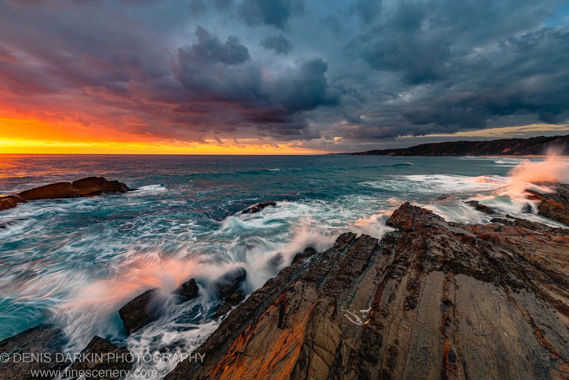 Long-exposure waves crash against striated coastal rocks in warm dawn light on the New South Wales south coast, December 2020.