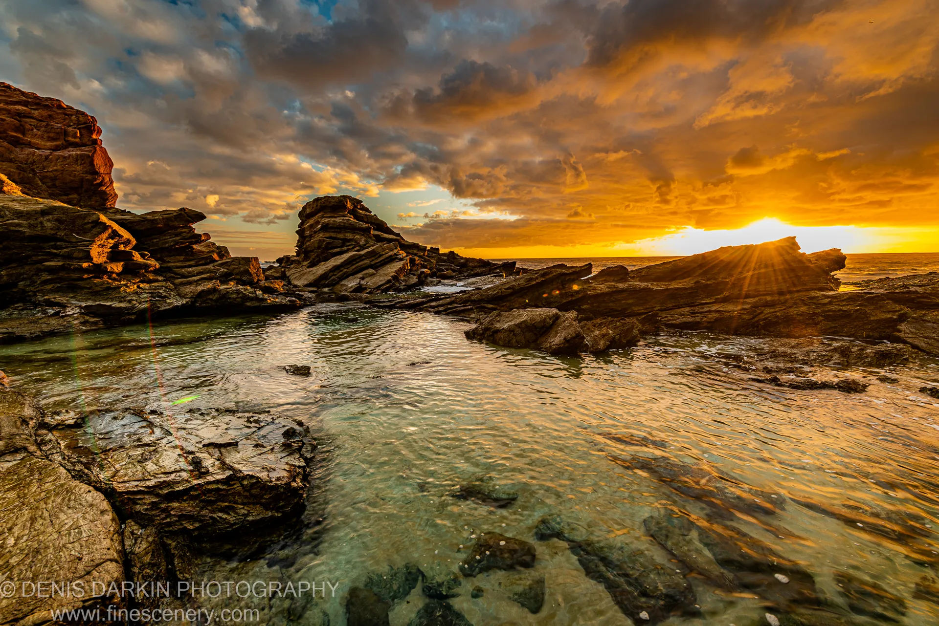 Golden rays breaking through a rock gap and falling on a clear tide pool at dawn on the South Coast, NSW.