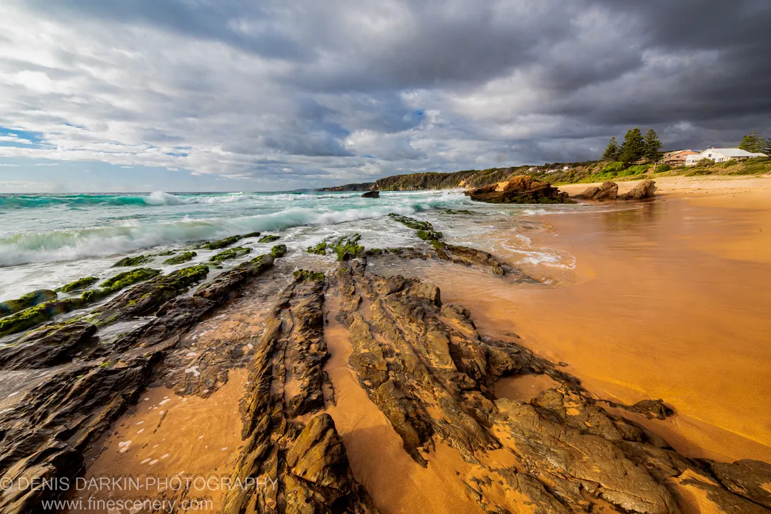 Layered moss-covered rock shelves lead toward distant cliffs on the South Coast, New South Wales, waves softened by long exposure.