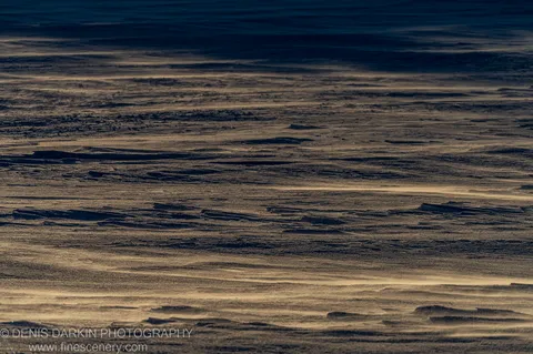 Vast frozen surface at Perisher Valley at golden hour, with deep blue-grey shadows contrasting with warm amber highlights on the undulating ice texture.
