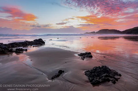 Tidal pools on a rocky Coffs Harbor beach at sunrise, pink and orange sky reflected in shallow water below a silhouetted headland.