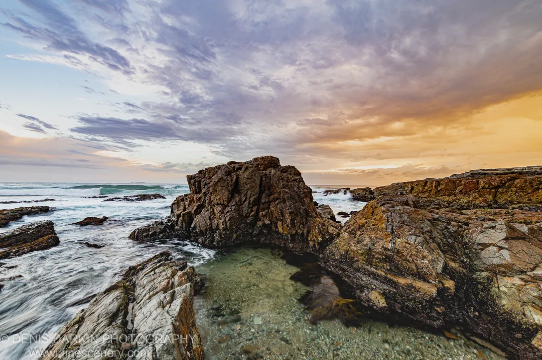 A natural rock pool in the foreground reflects the dusk sky above jagged coastal cliffs and long-exposure surf on the Coffs Harbor coast.