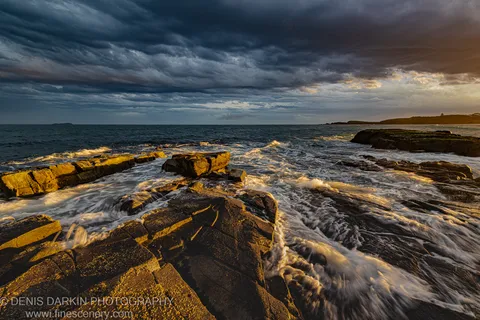 Barnacle-covered rocks on the Coffs Harbor coast at dusk, with storm clouds above and warm sunset light on the breaking waves.