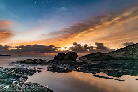 Smooth long-exposure waves on a rocky shore at pre-dawn near Nelson Bay, with moss-covered rock platforms and still tide pools in the foreground.