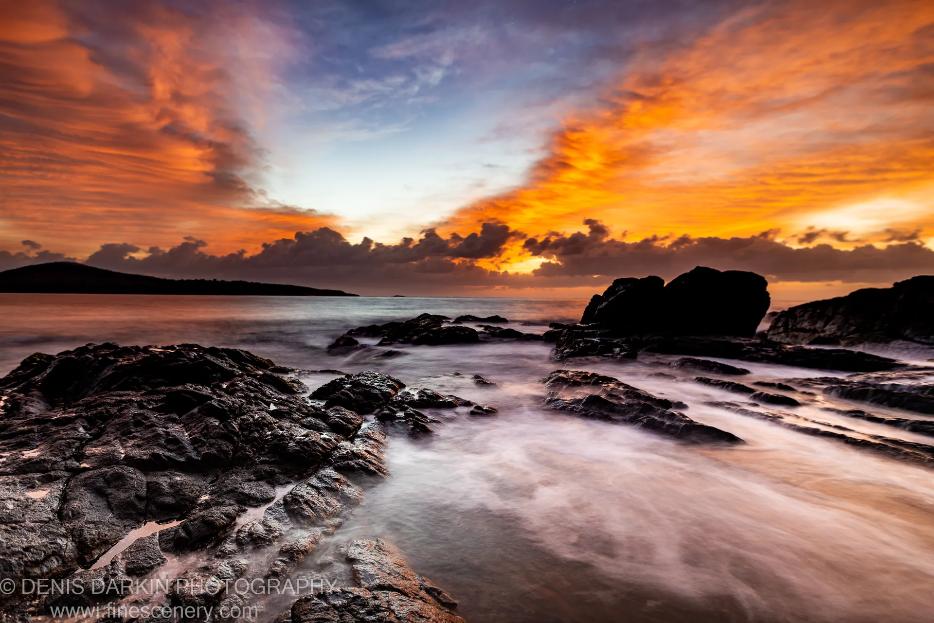 Jagged coastal rock formations at dawn near Nelson Bay, long-exposure water at their base and clouds lit in orange and violet tones above.