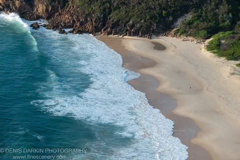 Wide sandy beach at Nelson Bay with wet sand in the foreground and rocky cliff faces at the shoreline under warm morning light.