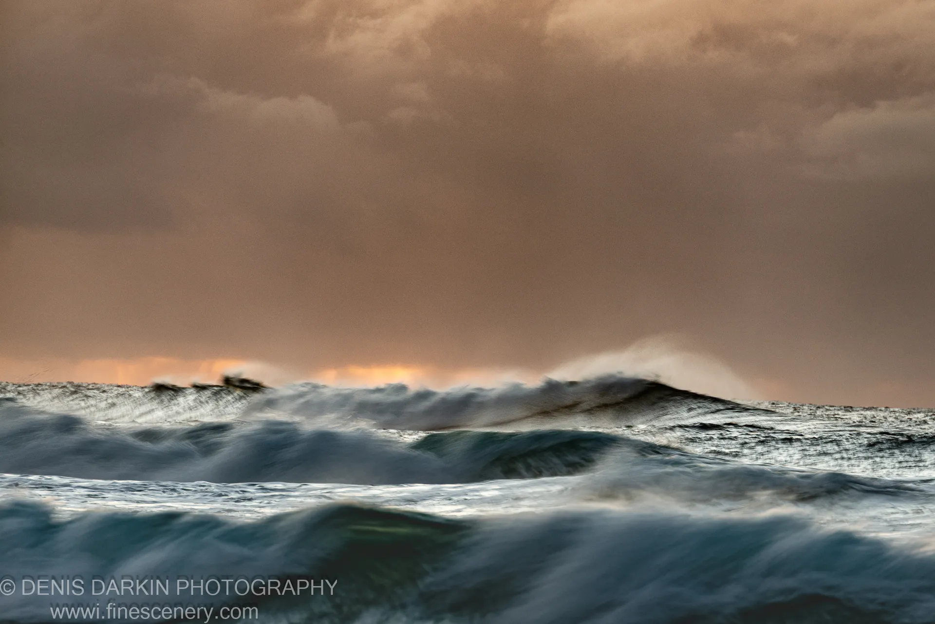 A breaking wave lit by amber light from a storm cloud gap at dawn, Byron Bay coast, NSW.