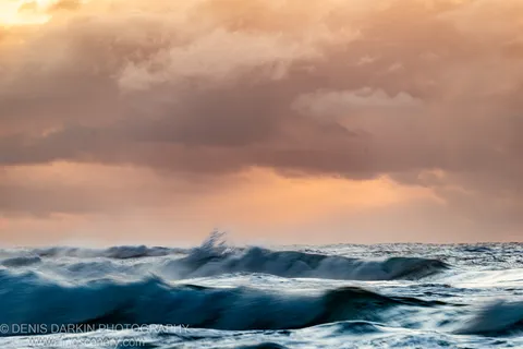 Long-exposure waves blurred into soft horizontal streaks below a heavy cloud canopy at dawn, Byron Bay coast, New South Wales, peach-toned sky above.