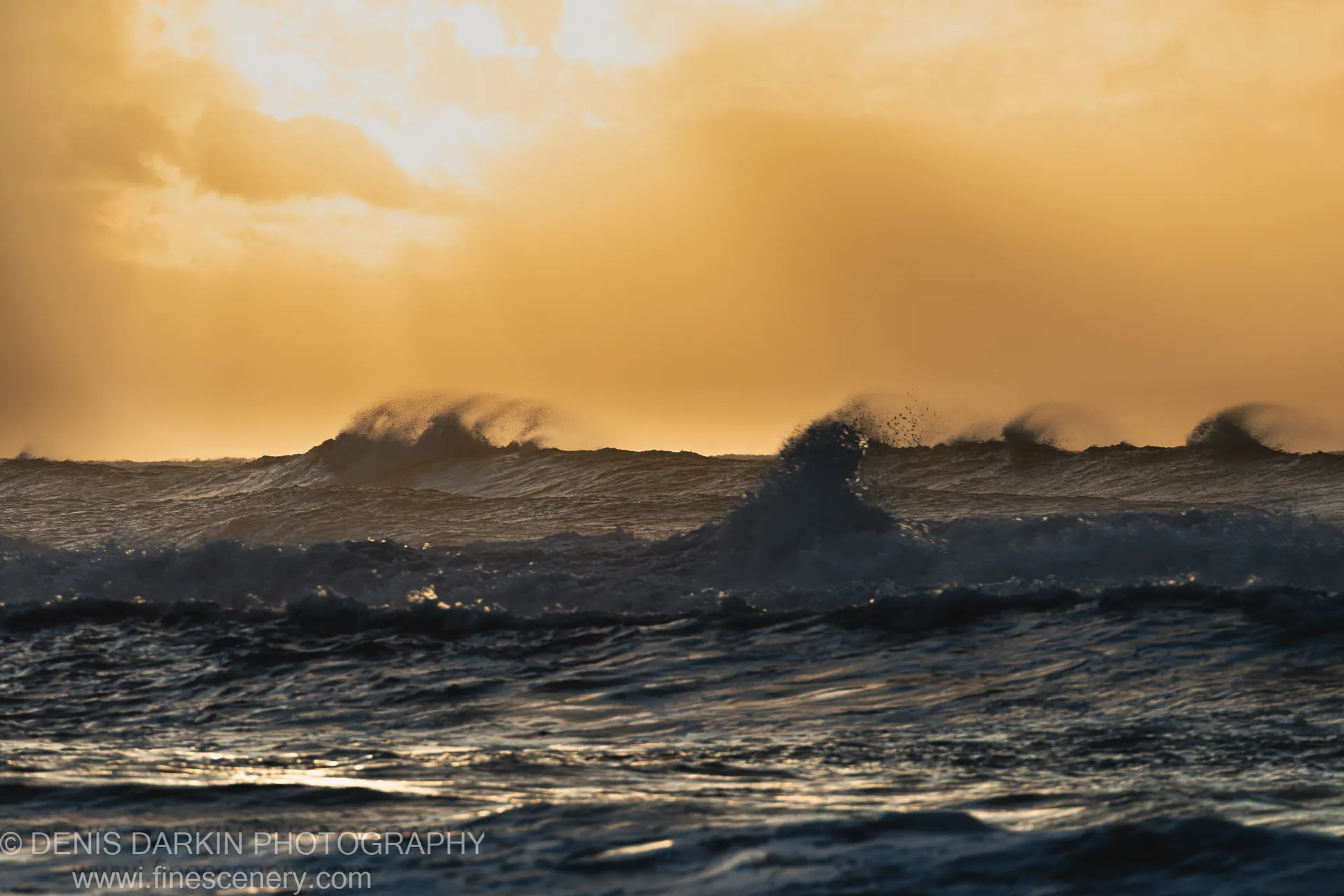 Telephoto view of breaking waves and backlit sea spray against a dark sky at dawn on the Byron Bay coast, New South Wales.