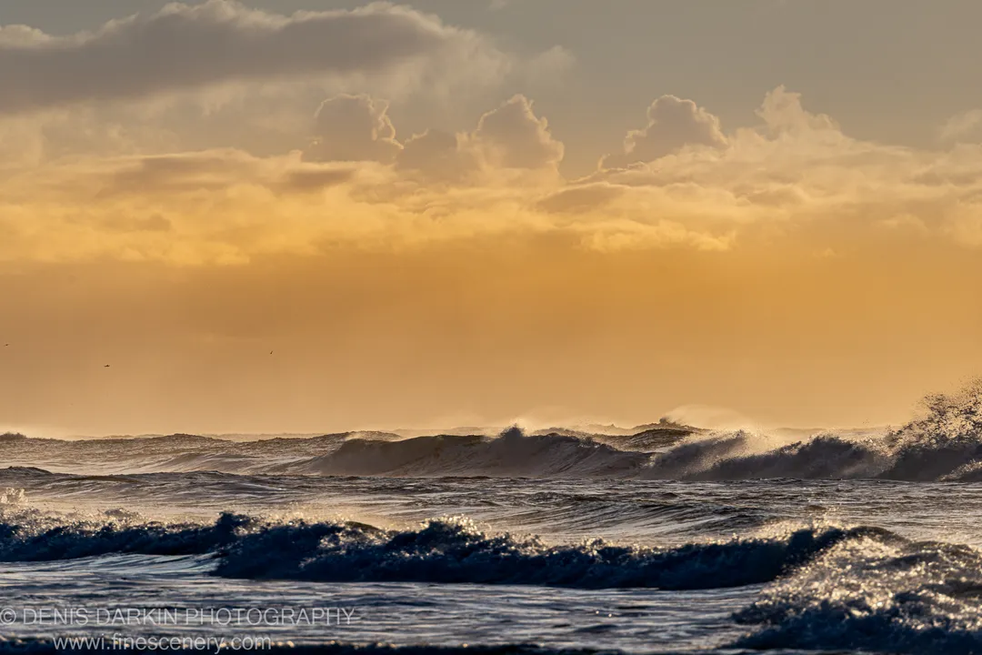 Breaking waves with white foam below amber cumulus clouds over the Byron Bay coast, NSW, winter morning.