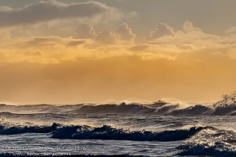 Breaking waves with white foam below amber cumulus clouds over the Byron Bay coast, NSW, winter morning.