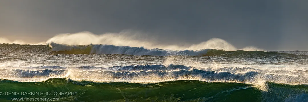 Low-angle winter sunlight backlights breaking sea spray against a dark grey sky at Byron Bay, New South Wales. June 2021.