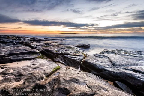 Weathered granite slabs with green moss on the New South Wales coast, long exposure smoothing the ocean at dawn.