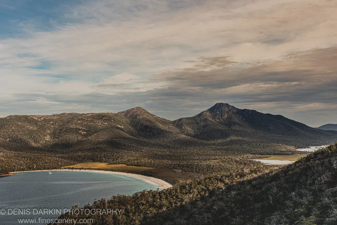Aerial view of Wineglass Bay showing the curved white beach and densely vegetated ridges in low late-afternoon light, East Coast Tasmania.