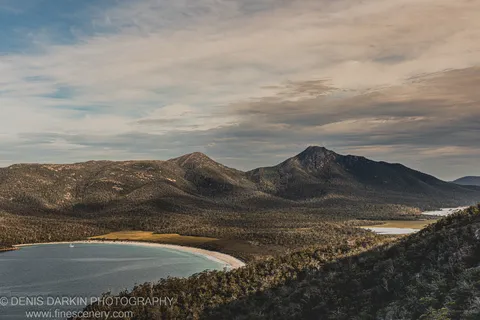 Aerial view of Wineglass Bay showing the curved white beach and densely vegetated ridges in low late-afternoon light, East Coast Tasmania.