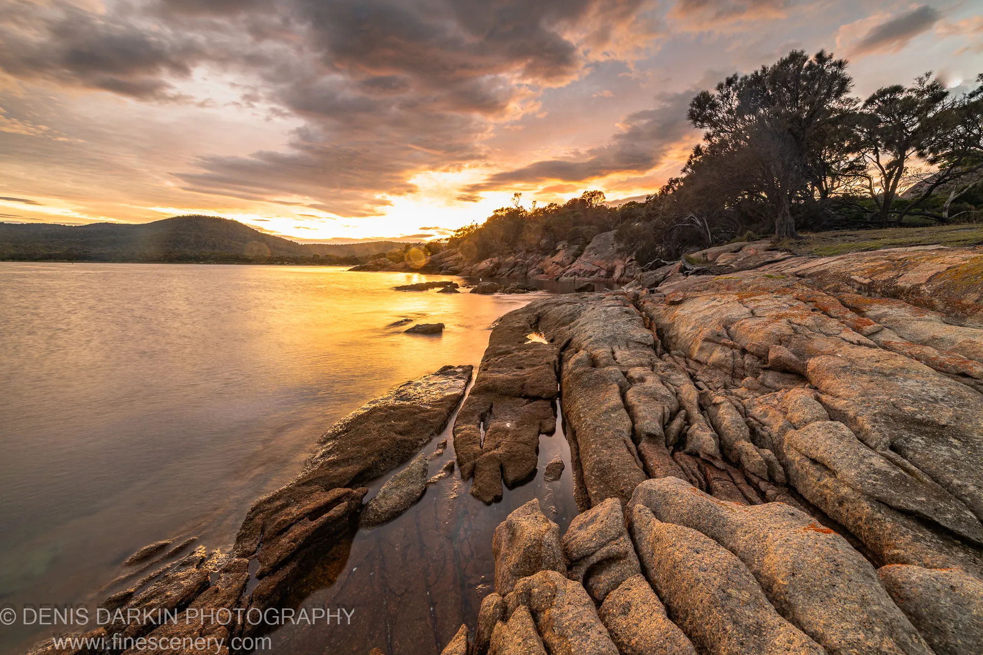 Smooth layered rock formations at Coles Bay, Tasmania, extend toward still long-exposure water below a textured cloud bank on an autumn morning.